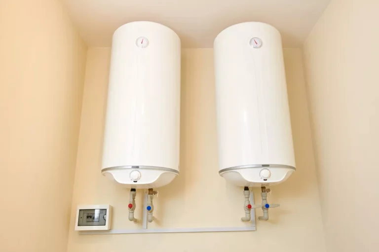 Two modern, cylindrical hot water heaters professionally mounted on a wall with organized red and blue plumbing fixtures and an electrical control panel.