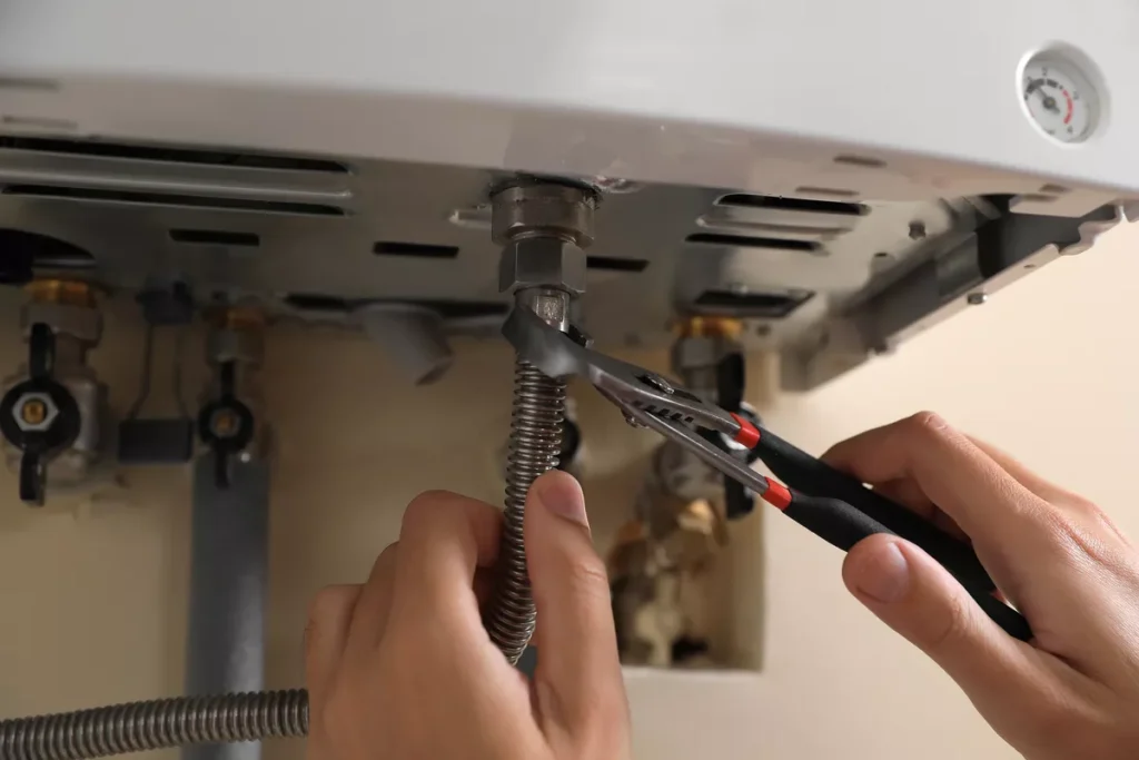 Close-up of a technician using pliers to secure a silver corrugated gas line connector to a white residential appliance.
