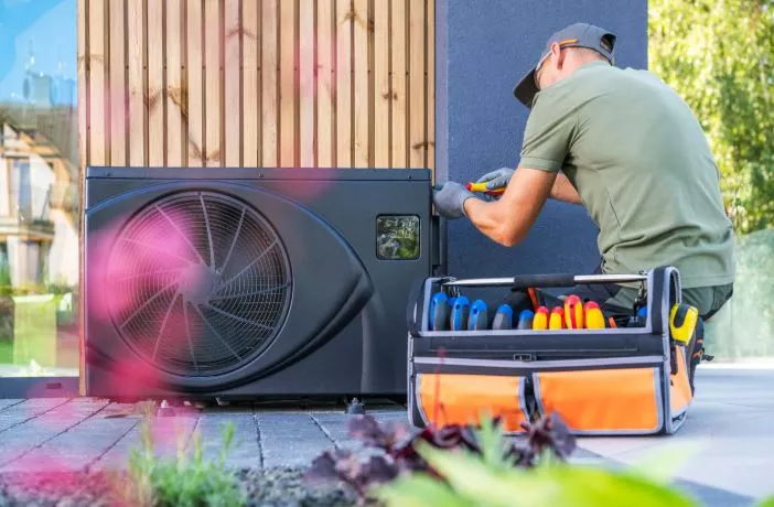Technician in a green shirt using tools from an orange toolbox to adjust an outdoor heat pump climate control unit.