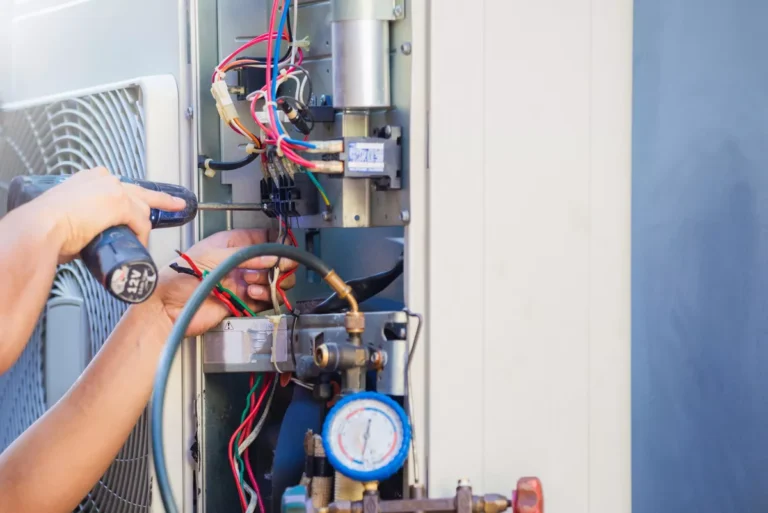 Close-up of a technician's hands using a screwdriver to repair internal wiring and electrical components of an air conditioning unit next to pressure gauges.