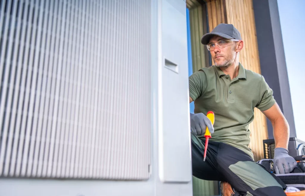 An experienced HVAC technician with gray hair and beard wearing safety glasses and gloves while performing a precision tune-up on an air conditioning unit.