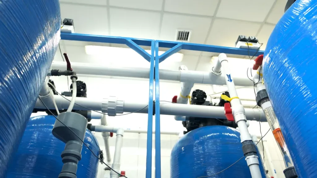 High-angle view of an industrial water treatment facility featuring a series of blue resin tanks and interconnected white PVC pipes.