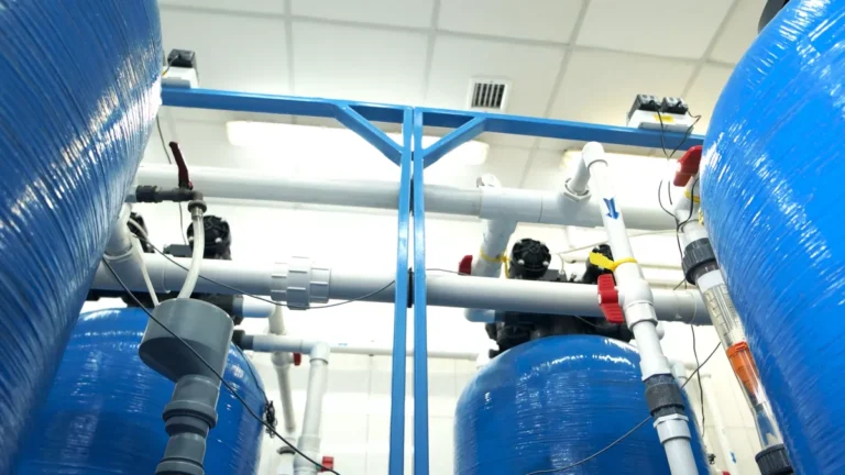 High-angle view of an industrial water treatment facility featuring a series of blue resin tanks and interconnected white PVC pipes.